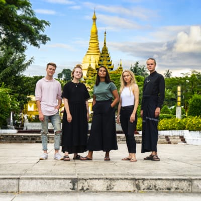 Viisi suomalaista nuorta poseeraa MyanmarinYangonissa temppelin edustalla.