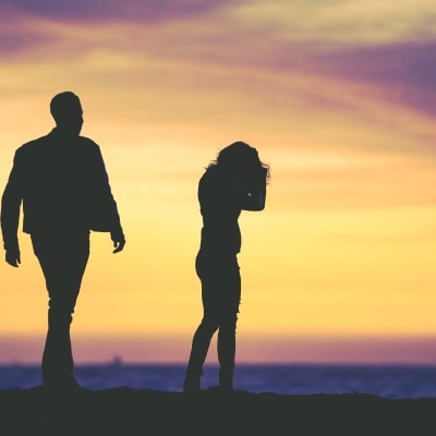 Mies ja nainen seisovat erillään auringonlaskussa.