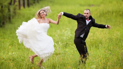 Man och kvinna i bröllopskläder hoppar upp i luften på grön äng
