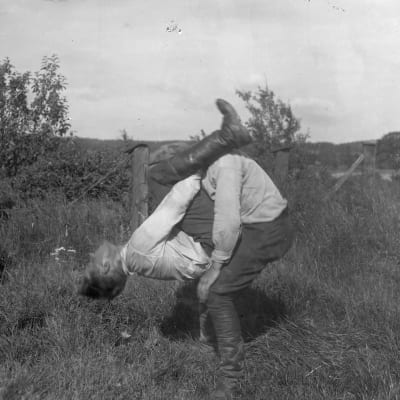 Två män leker leken "prova nacke", där den ena ska lyfta upp den andra med bara sin nackes styrka. Bilden är tagen 1930 i Bromarf.