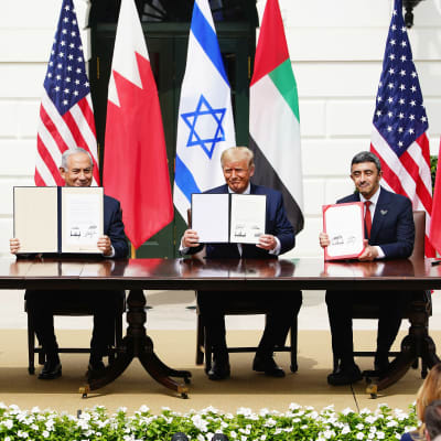 Vasemmalta Bahrainin ulkoministeri, Israelin pääministeri, Yhdysvaltain presidentti ja Arabiemiraattien ulkoministeri istuvat pöydän takana näyttäen yleisölle allekirjoitettuja sopimuksia, taustalla valtioiden lippuja