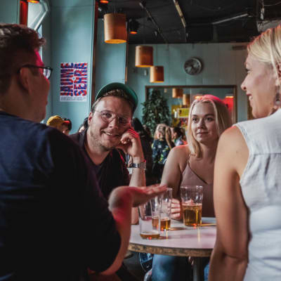 Två män och två kvinnor sitter vid ett restaurangbord och pratar och dricker öl.