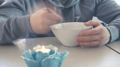 Huppariasuinen poika syö jotakin lautaselta, etualalla kynttilä.
