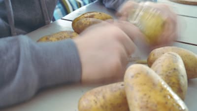 Kädet kuorivat perunoita.