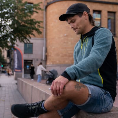 Ung man sitter på bänk i Helsingfors och tittar i sin telefon.