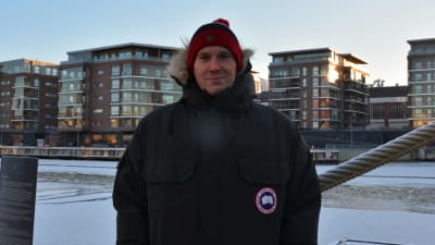 Porträtt av en man som poserar framför en frusen aura å. mannen är vinterklädd och bakom honom finns en tross mmed rimfrost över sig. 