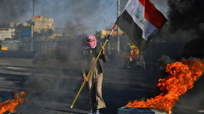 En demonstrant i Najaf, cirka 160 kilometer söder om Bagdad, bar på Iraks flagga bland brinnande bildäck på måndagen. 