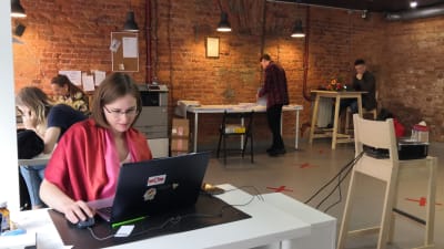 En kvinna sitter vid en dator i ett öppet kontorslandskap med röd tegelvägg.
