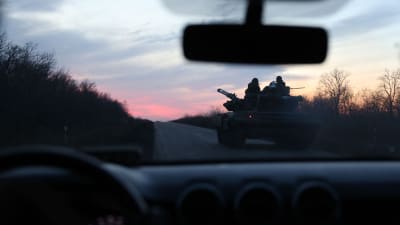 En ukrainsk stridsvagn syns genom ett bilfönster och kör mot en rodnande himmel med soldater i profil mot himlen.