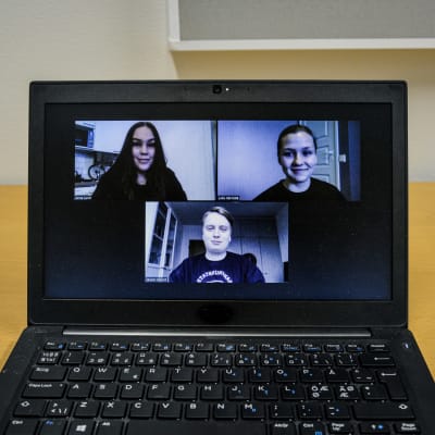 En laptopdator på ett bord. På skärmen syns tre unga personer i ett videosamtal.