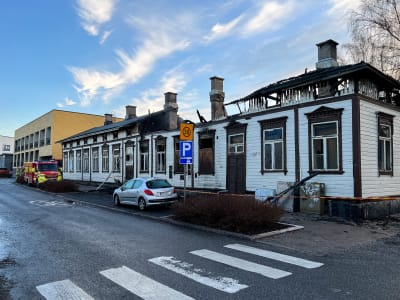 Ett svårt bränt vitt trähus i korsningen mellan Flemingatu och Linnankatu i Åbo. Husets tak har rasat in. Brandbilen står parkerad framför huset. Området är isolerat med en röd-gul tejp.