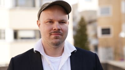 Jukka Haapakoski, en man i blå keps och vit kragskjorta under en mörk kavaj, är verksamhetsledare för de arbetslösa i Finland.