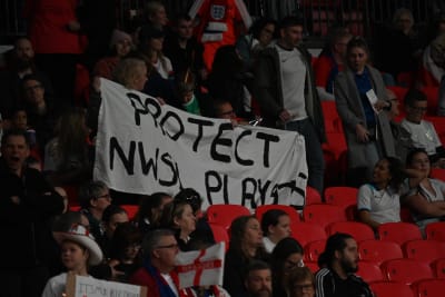 Fotbollsanhängare med en ställningstagande banderoll på läktaren. "Protect NWSL players" - skydda spelarna i NSWL