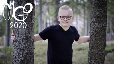 Kasper kikar fram mellan två trädstammar och tittar in i kameran