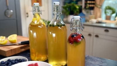Tre glasflaskor med gul kombucha i.