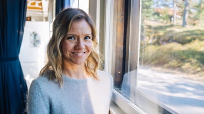 Sonja Kailassaari står vid ett fönster där ljuset strömmar in.