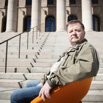 Vasemmistoliiton kansanedustaja Markus Mustajärvi istuu keltaisessa nojatuolissa Eduskuntatalon edessä.