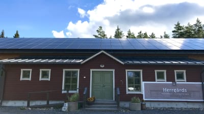 Röd byggnad med grön dörr. Solpaneler på taket. 
