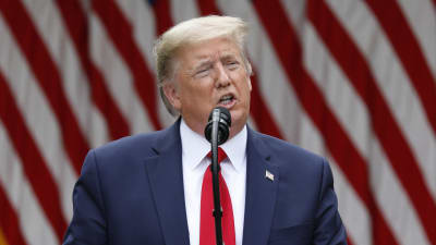 Donald Trump står vid ett talarpodium. I bakgrunden syns USA:s flagga.