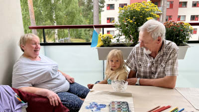 En glad farmor och farfar och ett treårigt barn på en balkong.