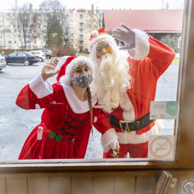 Tyttötonttu ja joulupukki vilkuttavat ulko-oven lasin takana.