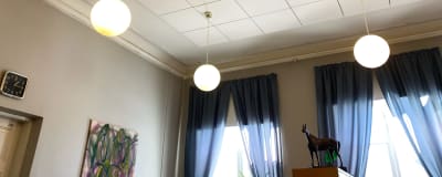 På bilden syns väggar och taket i ett kontor. Blå gardiner vid fönster, klotformade lampor hänger från taket. En häststaty står på ett skåp.
