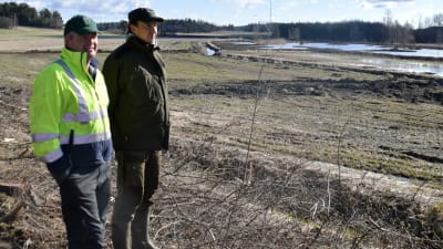 Anders Wasström och Ville Wahteristo står på en åker och blickar ut över en våtmark i Snappertuna.