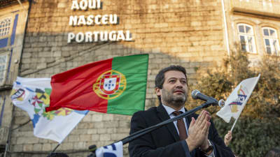Man står bakom mikrofon och i bakgrunden syns portugals flagga.