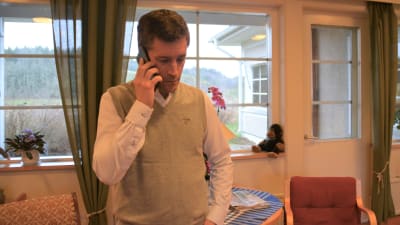 En man talar i telefon. Han finns i ett äldreboende (läkare, men civilt klädd)