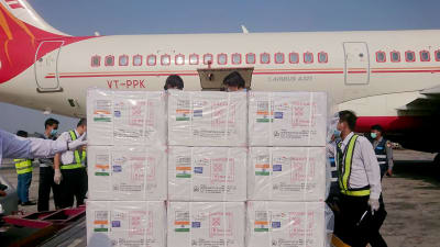 Lådor med markeringar som visar att de innehåller vaccin ligger på en lastpall framför ett flygplan med Air Indias beteckningar.
