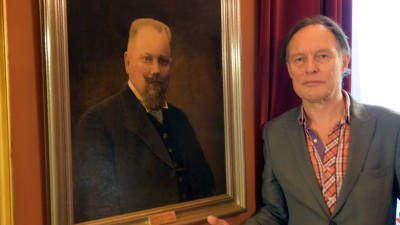 Konstnären Peik Bäckström står bredvid porträttet av borgmästare Harry Winqvist.