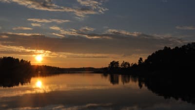 Ett spegelblankt hav med en sol som ligger strax ovanför horisonten och som speglar sig i havet. Öarna bildar svarta silhuetter.