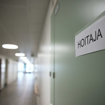 Terveyskeskuksen vaalea käytävä ja etualalla vihreä ovi jonka oveen on teipattu lappu jossa lukee hoitaja 9.