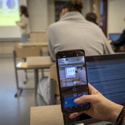 Lähikuva kännykästä joka kuvaa luokan edessä touhuavaa opettajaa salaa.
