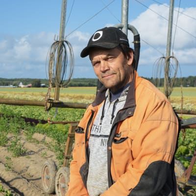 Jordbrukaren Christer Finne står på ett fält framför en bevattningsanläggning.