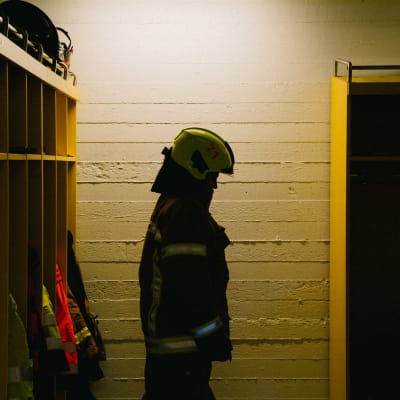 Palolaitoksen pukuhuoneessa seisoo henkilö palopuku päällä.