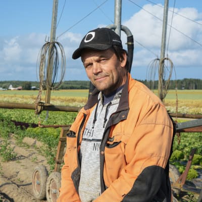 Jordbrukaren Christer Finne står på ett fält framför en bevattningsanläggning.