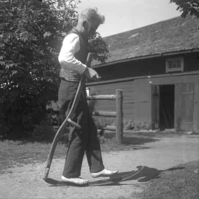 En man går barfota på en lie. Bilden är tagen 1931 i Ingå, Lill-Breds.
