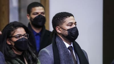 Jussie Smollett i munskydd utanför en domstol i Chicago. Han är klädd i en grå kappa, svart halsduk och svarta läderhandskar. 
