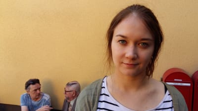 Emma Heino. I bakgrunden blir Kari Väänänen (Aulis Homelius) intervjuad.