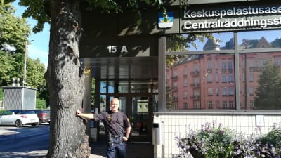 Brandmästare Vesa Berg står lutad mot ett trädd utanför Centralräddningsstationen i Berghäll.