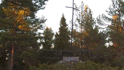 Monument av metall och sten som föreställer en båt med mast. Står bland träd i höstliga färger