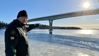 En sjöbevakare står och pekar ut mot isen under Emsalö bro.