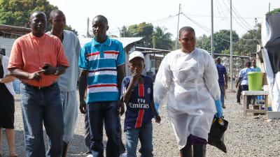 Nathan Gbotoe och hans son Abraham ( i mitten) smittades av ebola men överlevde. Här lämnar de sjukhuset i Liberia i december