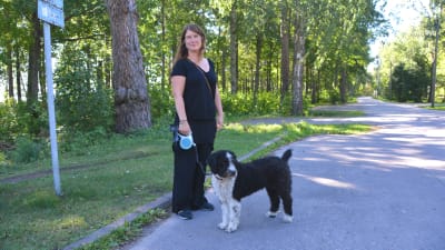 Sara Bengts står med svartvit hund i koppel vid vägen som går förbi Plagen