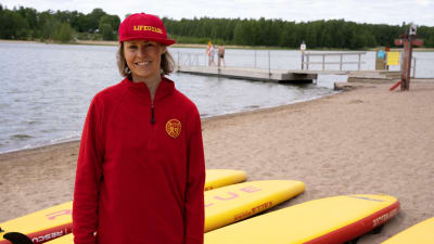 Riitta Vienola, utbildare inom livräddning på Finlands Simundervisnings- och Livräddningsförbund, FSL, står på badstrand framför räddningsbrädor.