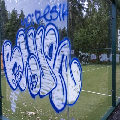 Graffiteja maalattuna padel-kentän plekseihin.