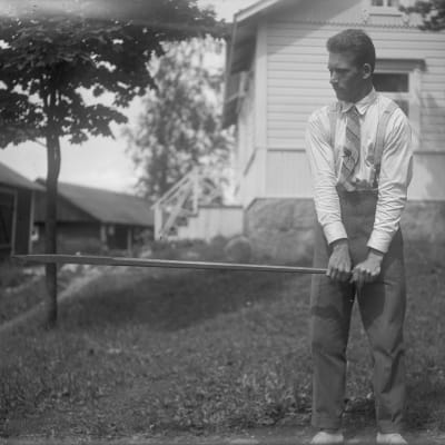 En man lyfter ett järnspett vågrätt. Bilden är tagen 1930 i Bromarf.