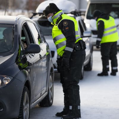 En gränsbevakare i vinterkläder och munskydd talar med en person i en bil,