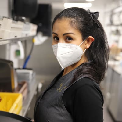 Ana Emilia Martinez Hale kasvomaskiin pukeutuneena katsoo kameraan ravintolakeittiössä.